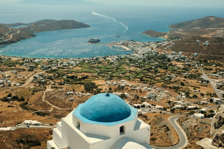 a white building with a blue dome and a blue dome on a hill overlooking a city and water Serifos Greece