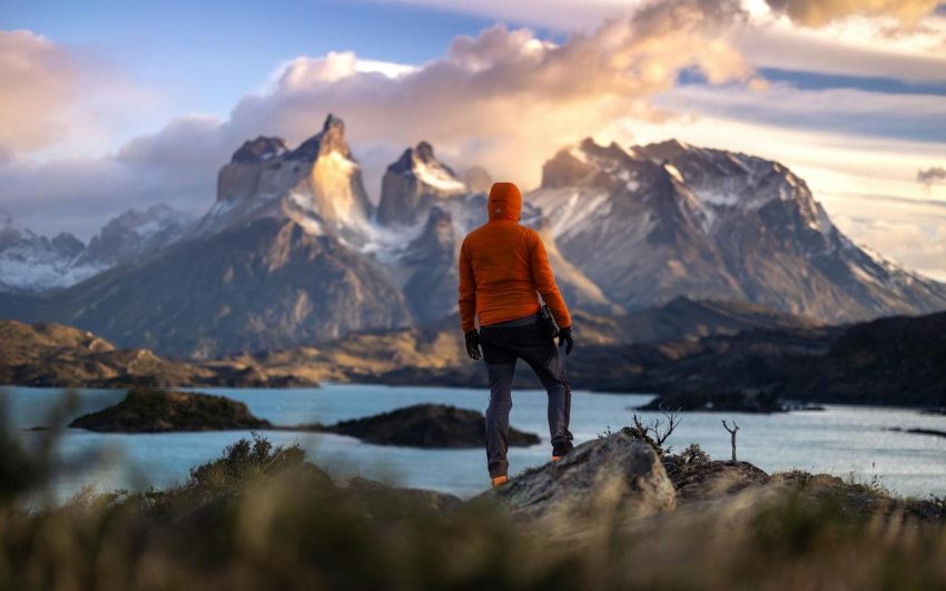 A hiker stands at sunrise in Torres del Paine, Chile, overlooking majestic mountains and a tranquil lake. Patagonia, Chile, Argentina