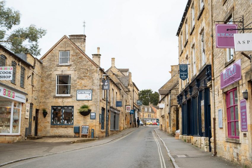 Picturesque village street in the Cotswolds, England featuring historic stone buildings and quaint shops.