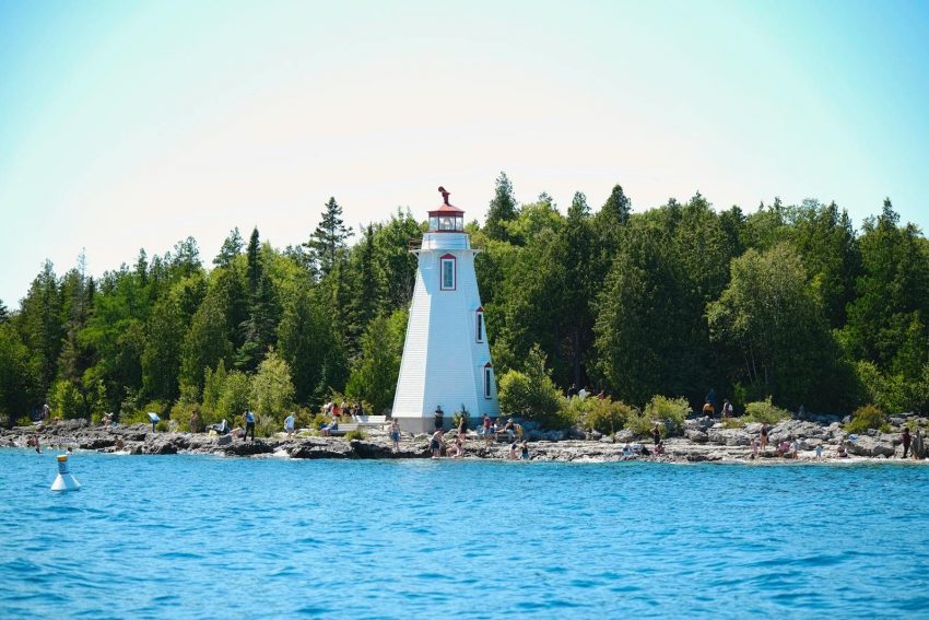 Beautiful lighthouse by vibrant shore, surrounded by trees and blue water.
