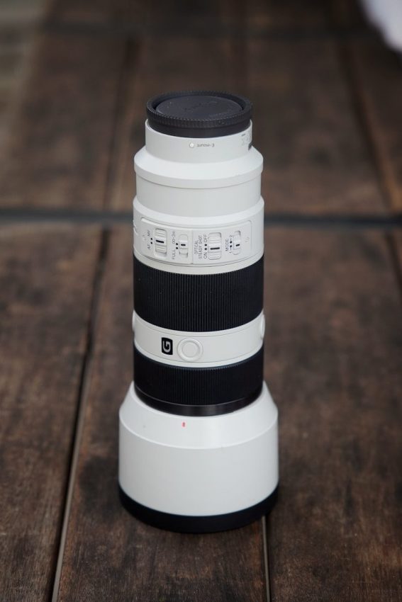 A white camera lens rests on a wooden surface.
