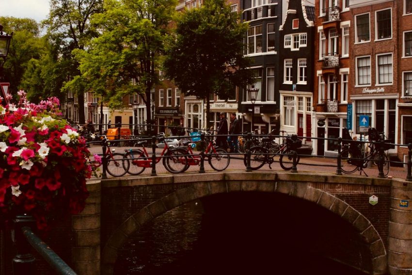 Scenic view of an Amsterdam canal bridge adorned with bicycles and vibrant flowers, perfect for urban travel inspiration.