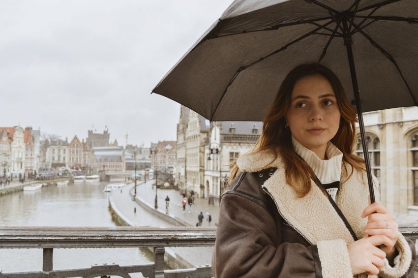 Woman with umbrella standing on a scenic European bridge during a rainy day.