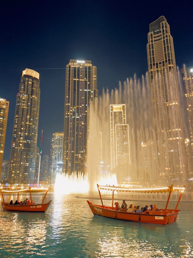 Captivating night view of Dubai's iconic fountain show with traditional boats and skyscrapers.
