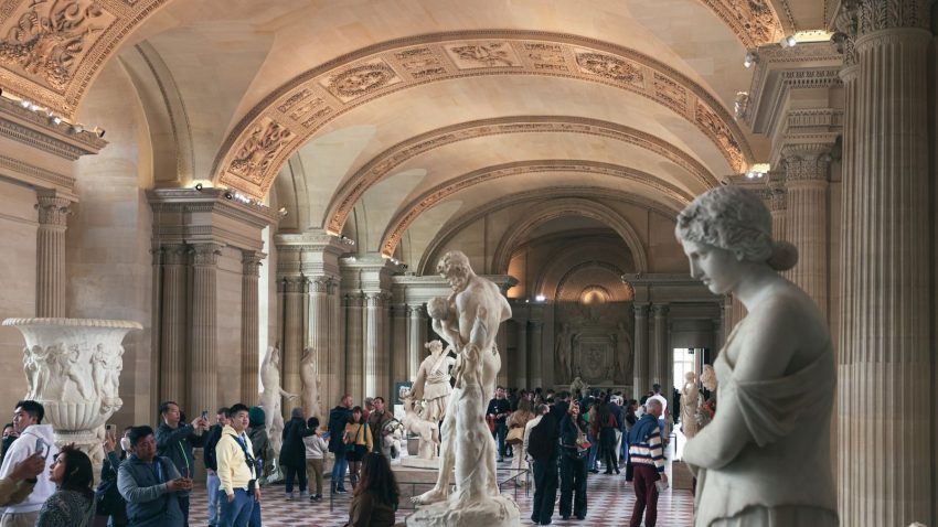 A crowded hall in the Louvre Museum, Paris, showcasing classical statues and architecture.