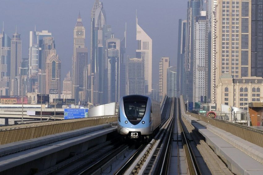 a silver train traveling down train tracks next to tall buildings, Dubai