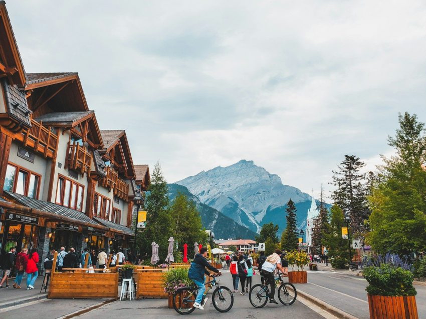 a group of people riding bikes on a street with a mountain in the background, Banff, Canada