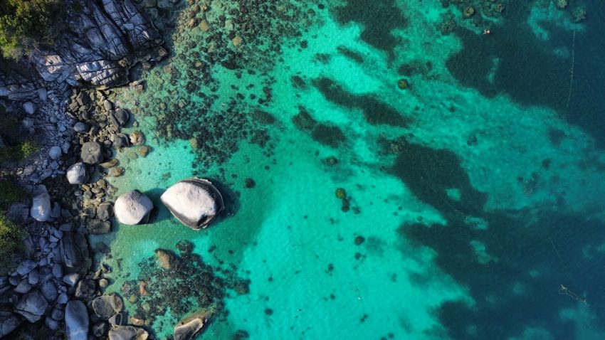 Breathtaking aerial view of turquoise waters and rocky shoreline in Ko Tao, Thailand.
