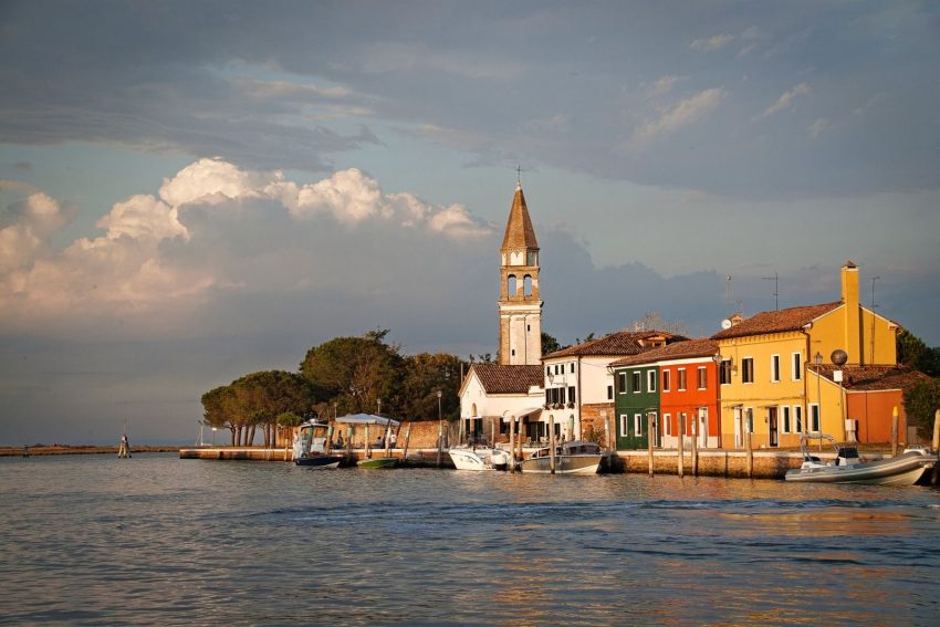 Colorful houses and a church by the canal on Burano island, a vibrant view at sunset. Pellestrina, Venice, Italy