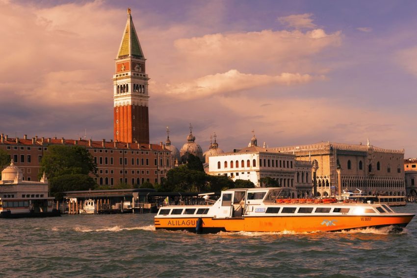 Scenic view of Venice canal featuring vaporetto and Campanile di San Marco at sunset.