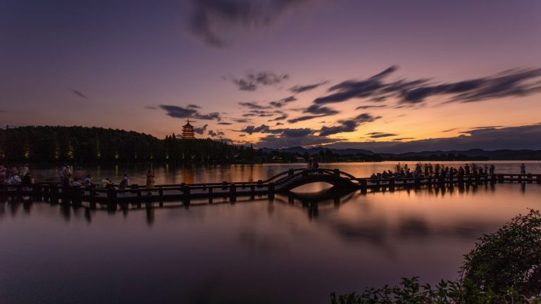 Serene twilight scene of West Lake in Hangzhou, showcasing a silhouetted pier and pagoda.