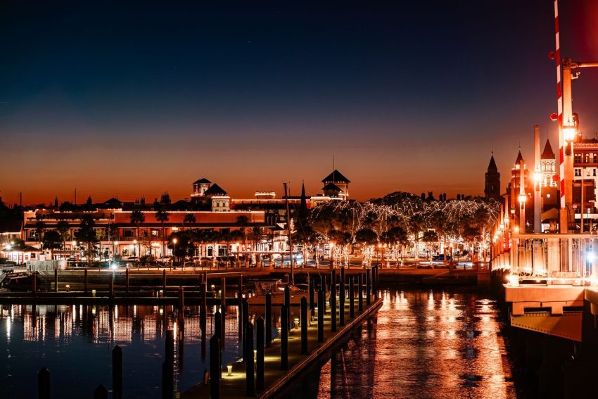 Beautiful nighttime view of St. Augustine Harbor, Florida, with lit buildings and boats reflecting on the water.
